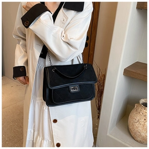 Detail of black quilted suede shoulder bag with metal turn-lock and chain strap