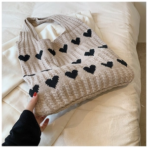 Détail du sac cabas en maille beige avec motifs de cœurs noirs et texture douce tissée
