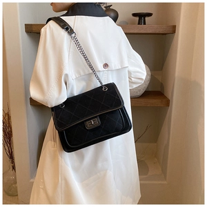 Detail of black quilted suede bag with metallic twist lock and chain strap on shoulder