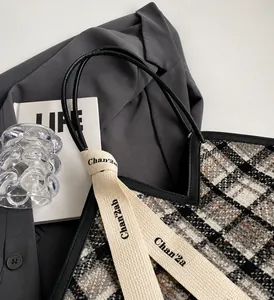 Detail of tweed tote bag with black leather cord handles and branded webbing straps
