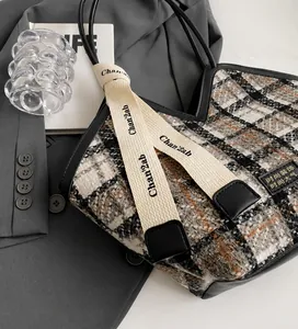 Detail of tweed checkered tote bag featuring leather trim and decorative ribbon