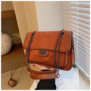 Detail of quilted suede shoulder bag in brick red with dark brown leather trim and metal lock