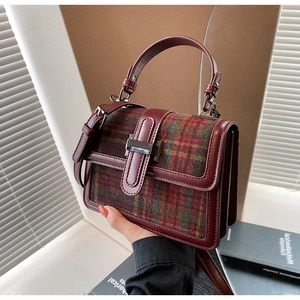 Detail view of burgundy leather and plaid tweed stitching on retro handbag with metal clasp