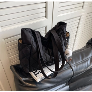 Detail of black quilted nylon tote bag with plush charm and side pocket on leather sofa