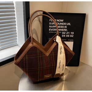 Detail of red and green plaid tote bag with brown leather handles and woven ribbon tag