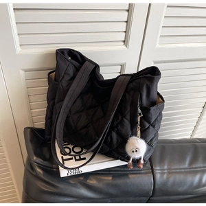 Detail of black quilted nylon tote bag with plush monster charm on a leather sofa