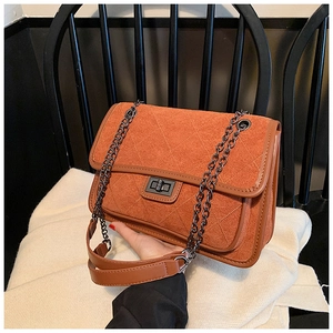 Detail of orange quilted suede bag with metallic twist lock and chain strap on knit rug