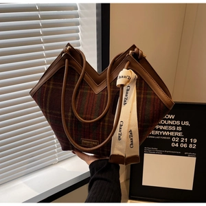 Detail of vintage plaid tote bag with brown leather handles and decorative woven strap