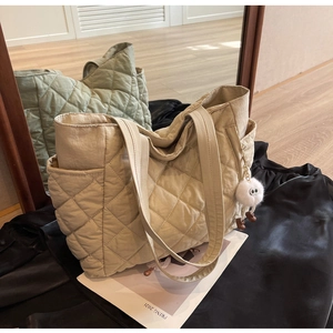 Detail of quilted beige nylon tote bag featuring diamond patterns and plush monster charm