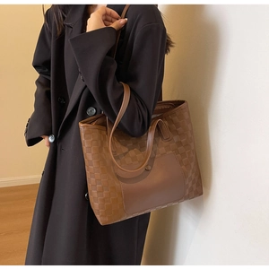 Detail of a large brown checkered tote bag worn with a black coat for daily commute