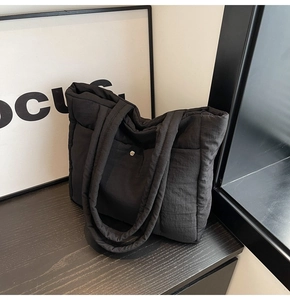 Close-up of black quilted nylon tote bag with silver buckle detail in minimalist setting