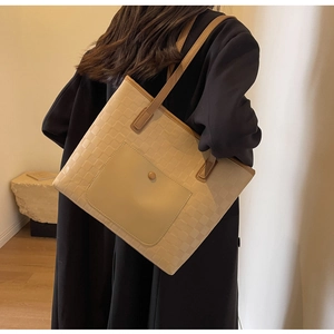 Detail of beige plaid tote bag with magnetic pocket and brown leather handles shown with coat