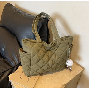 Close-up of dark green quilted nylon tote bag with plush charm and side pocket details