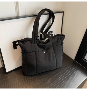 Detail of black quilted puffer tote bag with silver metal buckle and zipper closure
