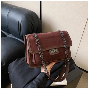 Detail of burgundy quilted suede texture with metal twist lock and chain strap on shoulder bag