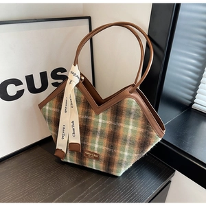 Detail of green-brown plaid tote bag featuring leather handles and V-shaped cutout