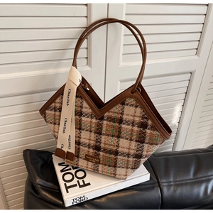 Detail of tweed tote bag with brown leather handles on white decorative books