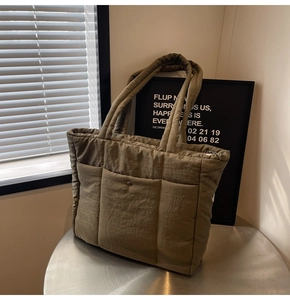 Close-up of olive green quilted nylon tote bag featuring front pockets and wide straps