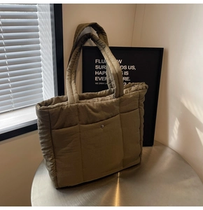 Detail of olive green quilted nylon tote bag with functional pockets on a metal table