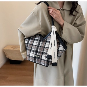 Detail of checkered tote bag with leather straps and decorative ribbon on shoulder