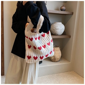 Détail de la texture tricotée et motif cœur rouge d'un sac cabas crème porté par un mannequin