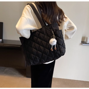 Detail of black quilted nylon tote bag with plush monster charm on model back view