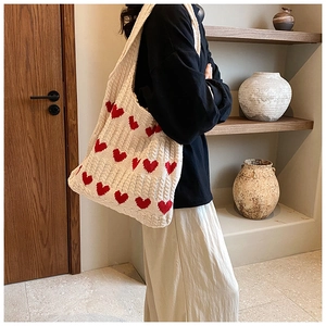 Détail du sac cabas en maille crème avec motifs de cœurs rouges porté à l'épaule