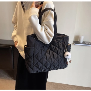 Detail of black quilted nylon tote bag with plush charm and side pocket on shoulder strap