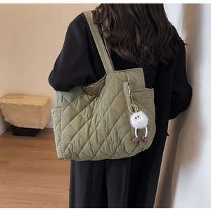 Green quilted nylon tote bag with plush charm accessory worn over black coat