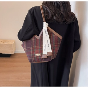 Detail of plaid canvas tote bag featuring brown leather trim and white decorative ribbon