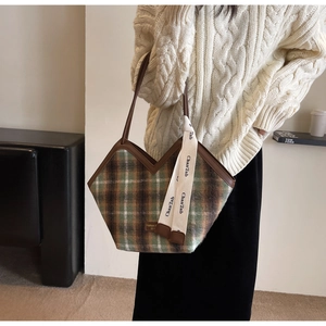 Close-up of V-shaped green plaid tote bag with brown leather trim and woven logo straps