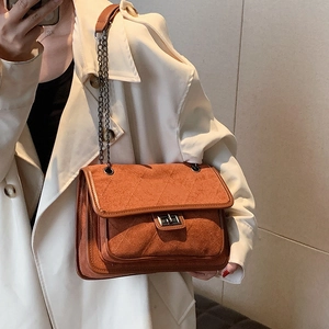 Quilted brown suede chain bag worn by a model in a beige trench coat for a chic look