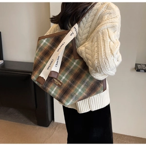 Close-up of tartan tote bag featuring wide canvas strap and premium leather brand patch