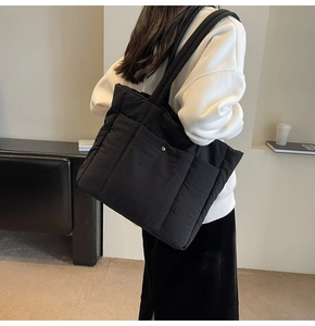 Detail of black quilted nylon tote bag with metal snap button and padded shoulder strap