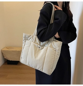 Detail of quilted puffer tote bag in off-white featuring functional front pocket and wide strap