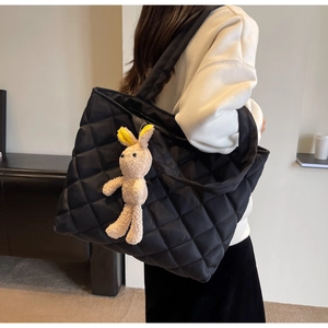 Detail of black quilted nylon tote bag with cute plush bunny pendant on shoulder strap