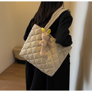 Detail of beige quilted nylon tote bag featuring a cute plush bunny charm and wide strap