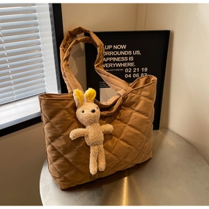 Detailed view of brown quilted nylon tote bag featuring a plush rabbit charm on a table