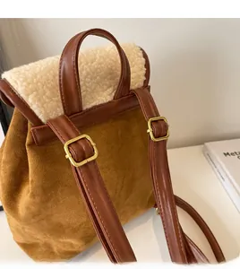 Detail of adjustable brown leather straps with gold buckles on a suede backpack