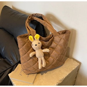 Detail of brown quilted nylon tote bag with decorative plush rabbit charm on a stone base