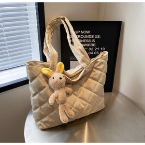 Detailed close-up of beige quilted nylon tote bag with a plush rabbit charm on a table