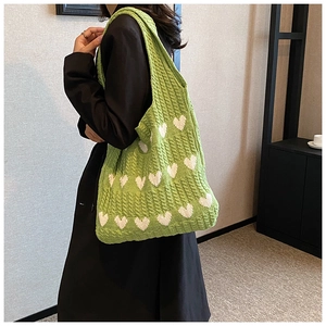 Détail du cabas en tricot vert avec motifs de cœurs blancs porté par un mannequin en manteau
