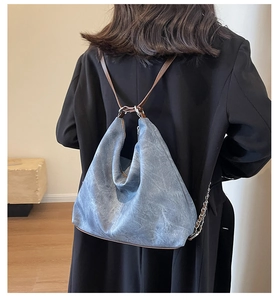 Detail of the large denim hobo backpack showing grey-blue texture and side chain