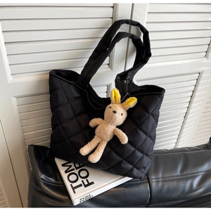 Detail of black quilted nylon tote bag featuring a cute plush bunny charm and diamond pattern