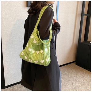 Détail d'un sac cabas en tricot vert avec motifs de cœurs blancs et texture douce