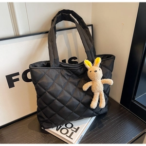 Close-up of black quilted nylon tote bag with plush bunny charm and wide shoulder straps