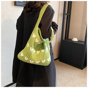 Vue d'épaule d'un grand sac cabas en tricot vert avec motif de cœur blanc