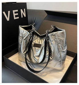 Close-up of silver quilted tote bag featuring a black fashion label and chain strap detail