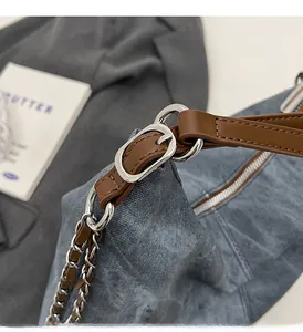 Detail of denim bag with brown leather strap and silver metal chain hardware
