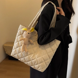 Quilted beige nylon tote bag with plush bunny charm shown on model shoulder